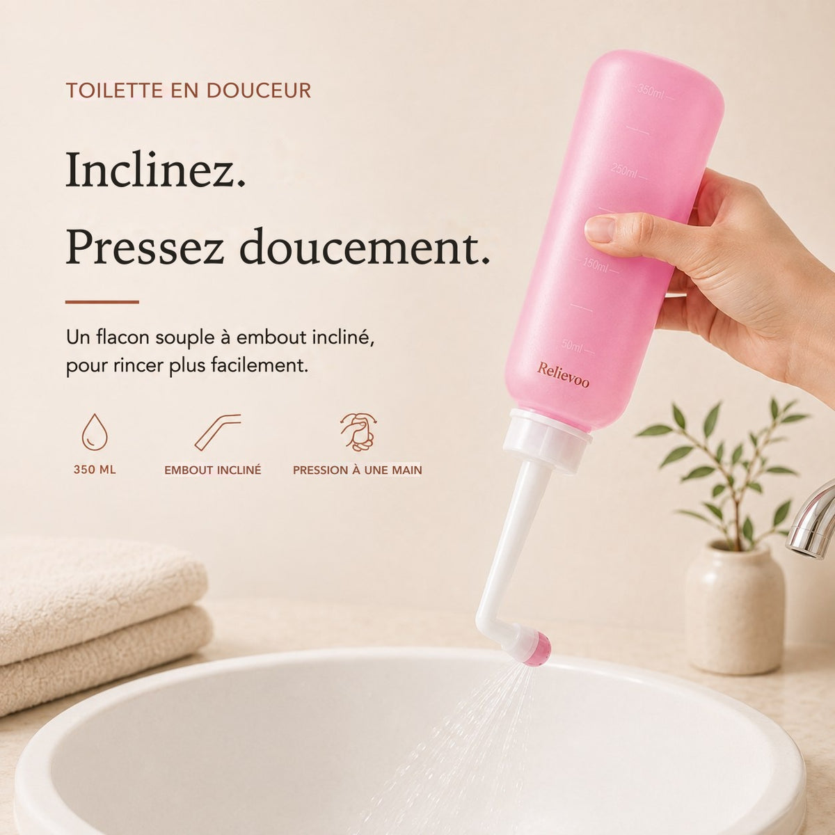 Main pressant le flacon rince-périnée rose Relievoo de 350 ml à embout incliné au-dessus d’une vasque