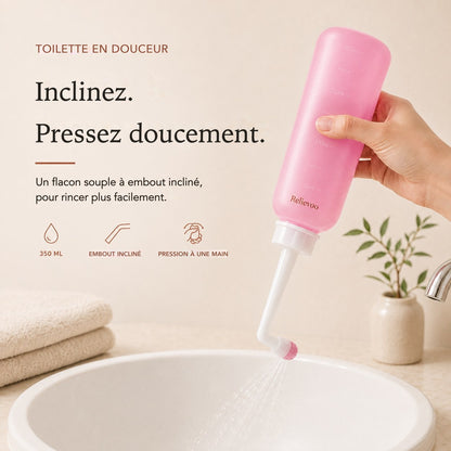 Main pressant le flacon rince-périnée rose Relievoo de 350 ml à embout incliné au-dessus d’une vasque