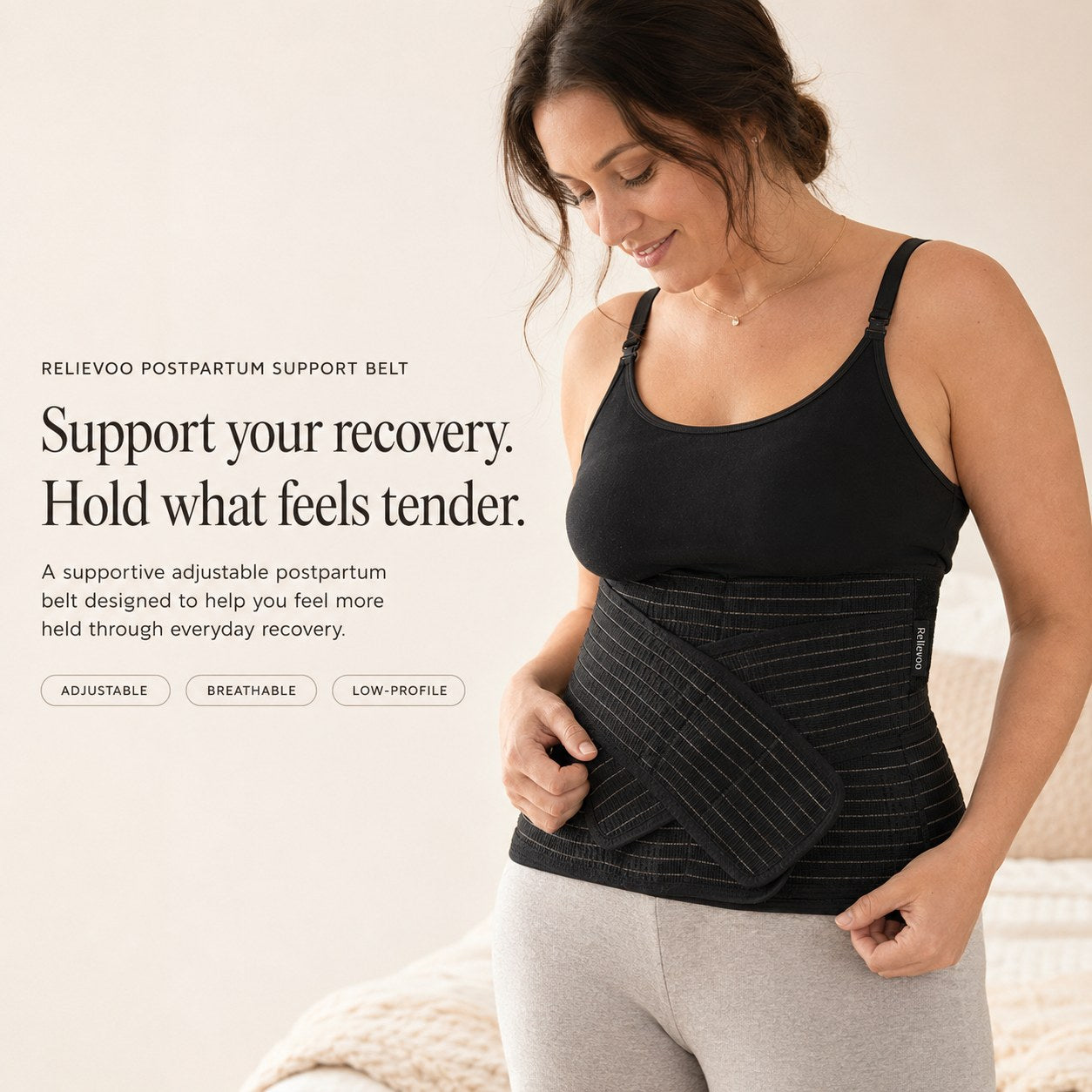 Woman wearing the black Relievoo postpartum support belt over a black vest top, holding the front support strap