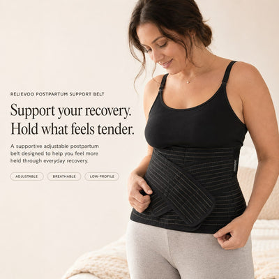Woman wearing the black Relievoo postpartum support belt over a black vest top, holding the front support strap