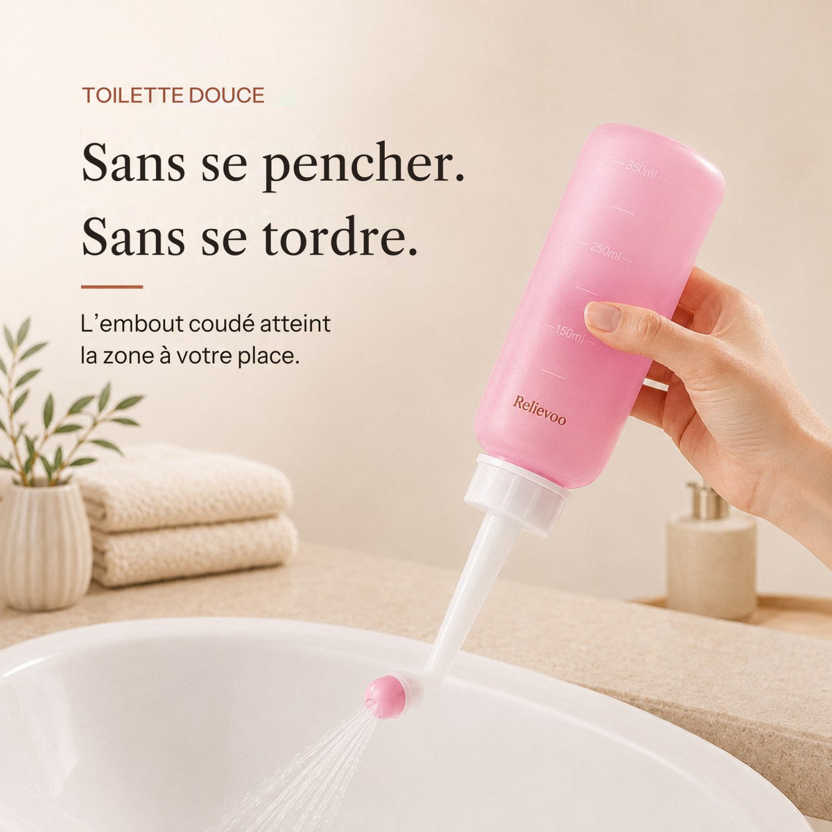 Main tenant le flacon rince-périnée rose Relievoo de 350 ml avec son embout coudé au-dessus d’un lavabo