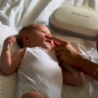 Smiling baby lying on the bed next to the Relievoo M22 PRO2 carry case while mum strokes their cheek after a pumping session