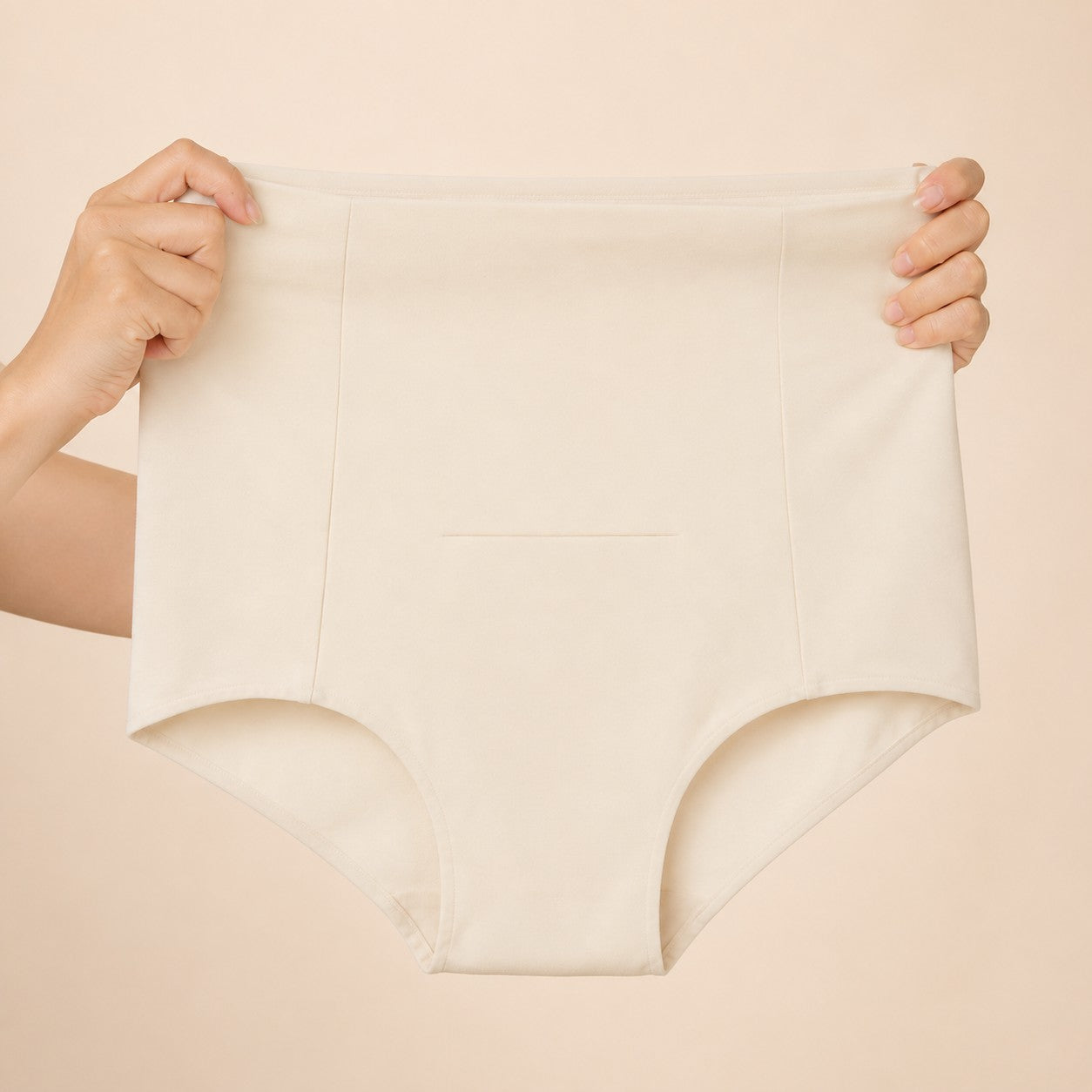 Hands stretching the ivory postpartum soothing briefs to show the soft four-way stretch fabric