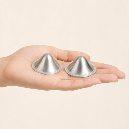 A pair of small silver nursing cup domes resting across a mother's open fingers, showing their true scale