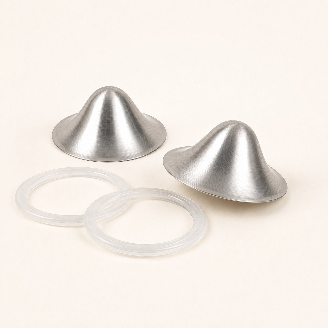 Two brushed silver nursing cups photographed at an angle beside their two clear silicone sealing rings