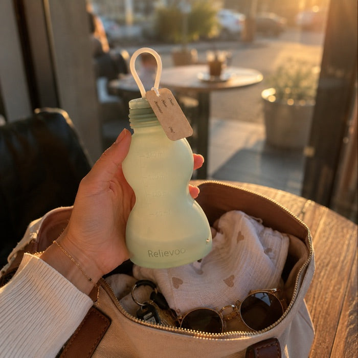 Relievoo reusable silicone milk storage bottle lifted leak-free from a changing bag at golden hour