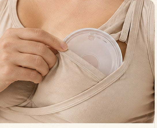 Hand slipping a Relievoo breast milk collector inside a nursing bra